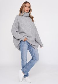 Szary, oversize sweter z golfem, żebrowana struktura, w zestawie z jasnoniebieskimi prostymi dżinsami i białymi sneakersami, na jednolitym tle.
