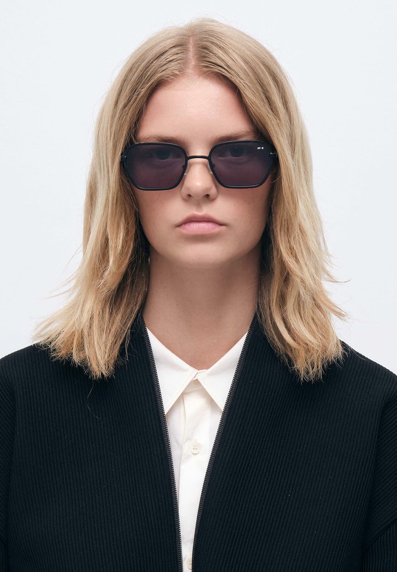 Sorte solbriller med rektangulær form og mørke linser. Har et minimalistisk design med en tynd ramme i sort metal.