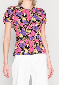 Haut à imprimé floral avec manches bouffantes dans des tons de rose, violet, orange et noir. Le tissu semble léger avec une texture lisse.