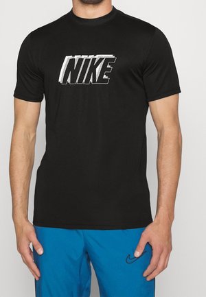 Homme portant un t-shirt Nike noir avec un grand logo et un short bleu avec un petit swoosh Nike sur la cuisse droite.