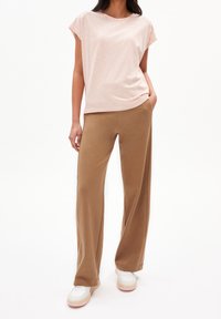 T-shirt rayé rose clair à manches courtes associé à un pantalon large beige. Des baskets blanches avec des accents roses complètent le look.