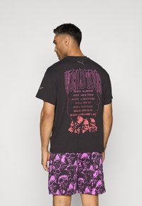 Sort t-shirt med "WORLD TOUR" grafik i rød og lilla, parret med lilla shorts med et kranie mønster. Begge dele er afslappede og i løs pasform.