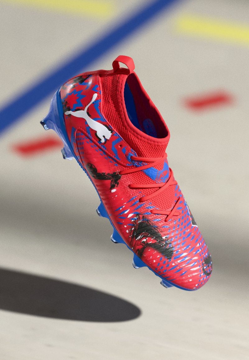 Botte de football rouge avec des accents bleus, tige texturée et motifs graphiques. Présente un col de style chaussette et une semelle à crampons pour une meilleure adhérence.