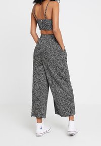 Svart och vit prickig crop top som är matchad med vida byxor. Outfiten har en avslappnad passform och tunna axelband. Bärs med vita sneakers.