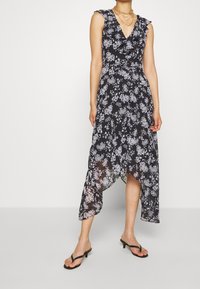 Black floral dress with ruffled neckline, asymmetric hem, and sleeveless design. Fabric is lightweight with a flowy texture. Accented with white flowers.