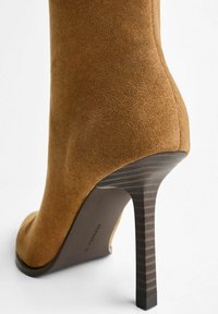Bottines à talons hauts en daim marron avec un bout pointu et un design de rayure noire texturée sur le talon. Fini lisse et silhouette courbée.