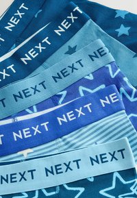 Pile de six sous-vêtements bleus pour garçons avec différents motifs d'étoiles et de rayures, et des ceintures étiquetées "NEXT" en lettres capitales.