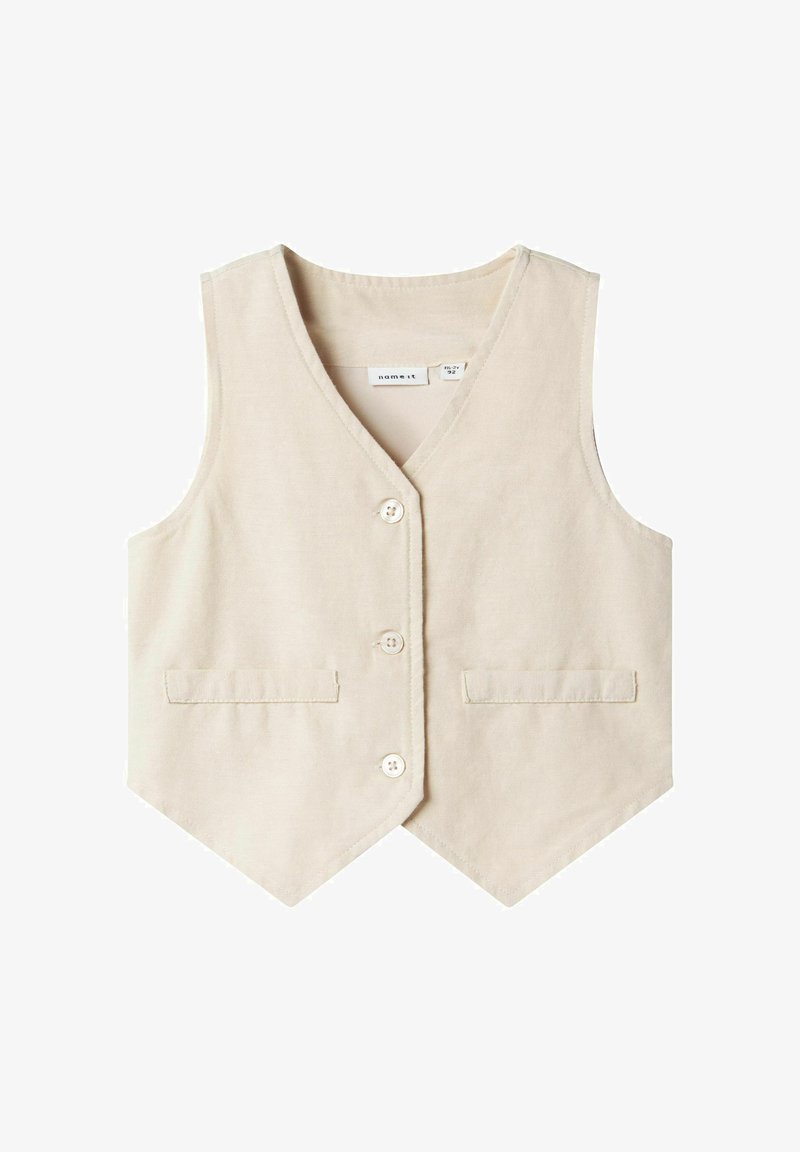 Bežs kokvilnas veste ar V veida izgriezumu, piecām pogām un divām priekšējām kabatām. Gluda tekstūra ar piegriezumu un smailu apakšmalu.