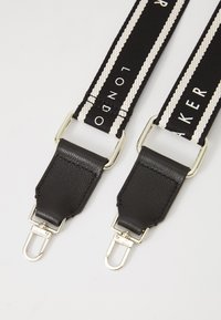 Cinghia in webbing bianca e nera con estremità in pelle; presenta accessori in argento e la parola "LONDON" in lettere bianche lungo la cinghia.