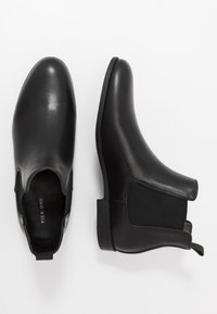 Bottines en cuir noir avec panneaux latéraux élastiques, texture lisse, bout arrondi et languette au talon pour un enfilage facile. Semelle plate en caoutchouc.