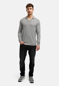 Grå långärmad skjorta med V-ringad krage, ribbade ärmslut och fåll. Matchad med svarta jeans och grå sneakers.