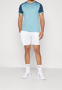 Camiseta de Nike de manga corta azul claro con detalles en azul marino, combinada con pantalones cortos blancos que presentan un logo negro; calcetines blancos y zapatillas completan el atuendo.