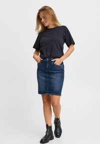 Černé tričko s krátkým rukávem a jemnou ozdobou, spárované s těsným kadenčním sukněm z tmavého denimu a černými kotníkovými botami.