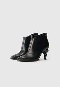 Black leather ankle boots with a pointed toe, shiny texture, and a unique low sculptural black heel. Features a side zipper for easy wear.