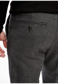 Detailní záběr na osobu, která má na sobě černobílé kostkované kalhoty s knoflíkem na zadní kapse a černé tričko viditelné v pase.