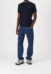 Granatowy bawełniany t-shirt z okrągłym dekoltem, uzupełniony jasnoniebieskimi dżinsami i szarymi butami sportowymi z czarnymi akcentami.