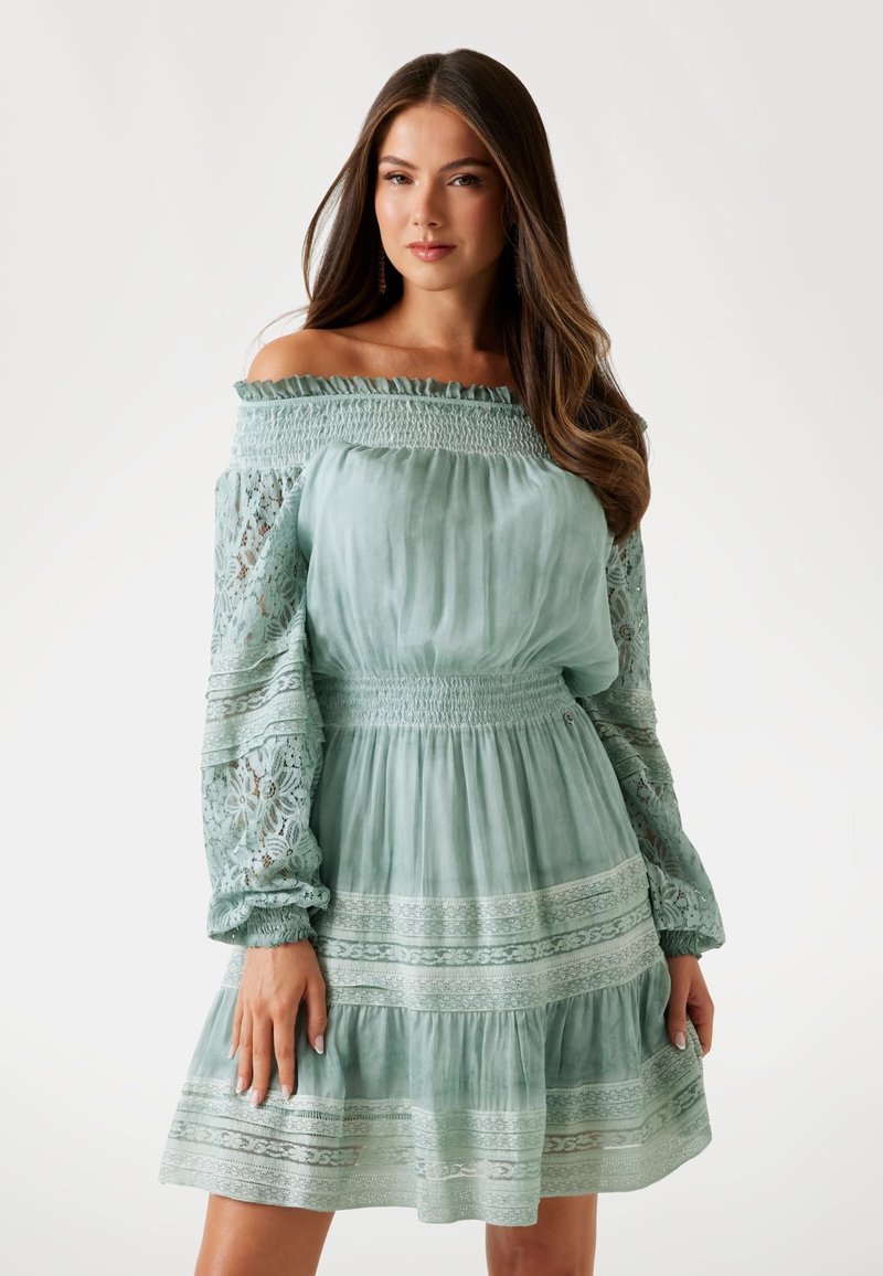 Hellgrünes Off-Shoulder-Kleid mit Spitzenverzierungen, gerafftem Bund, langen Puffärmeln und gestuftem Rock. Strukturierter Stoff und dekorative Details.