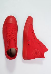 Un paio di sneaker alte rosse brillanti con lacci e suole in gomma, una vista dall'alto e l'altra di lato con il patch del logo.