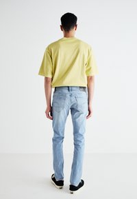 Ljusgul oversized t-shirt i bomull och ljusblå raka jeans. Jeansen har bakfickor och en svart etikett på midjebandet. Svarta sneakers.