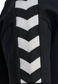 Sort beklædningsgenstand med en tekstureret, sort og hvid chevron-stribet detalje. Stoffet har en glat, mat finish med kontrasterende mønstre.