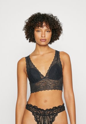 Zwarte kanten bralette met V-halsontwerp en golvende randen, gecombineerd met een bijpassende kanten string met bloemmotieven en decoratieve accenten.