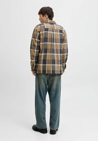 Camicia di flanella a scacchi nei toni del marrone, grigio e bianco; vestibilità rilassata con polsini abbottonati. Abbinata a jeans larghi e sbiaditi di colore blu e scarpe nere.