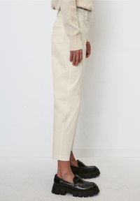 Beige Hochbundhose mit geradem Schnitt, Seitentaschen und glatter Oberfläche, kombiniert mit schwarzen klobigen Mokassins.