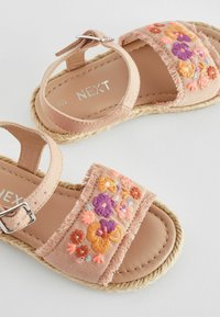 Rosa Stoffsandalen mit gestickten Blumen in Orange, Lila und Pink. Mit ausgefranstem Rand, verstellbarem Riemen und geflochtener Jutesohle.