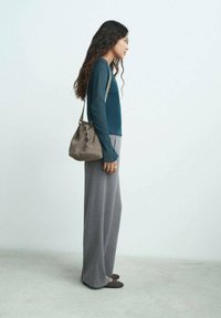 Top de manga larga color teal combinado con pantalones grises sueltos. Los pantalones tienen adornos laterales. Un bolso cruzado de ante gris complementa el atuendo.