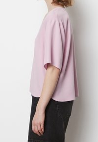 Blusa rosa a maniche corte con vestibilità ampia, caratterizzata da un collo a V e un tessuto morbido. Indossata con pantaloni corti neri a vita alta.