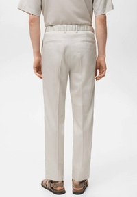 Relaxed-fit beige trousers with an elastic waistband, two back pockets, and a smooth texture. Paired with brown sandals.