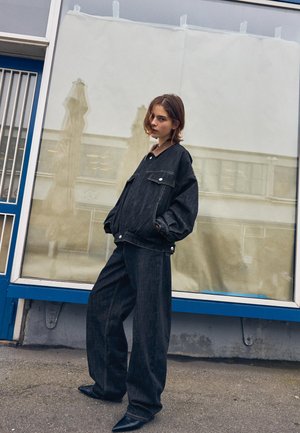 Tmavé džínsové oversized sako s dvoma prednými vreckami a zapínaním na gombíky, v spojení so širokými nohavicami, doplnené špicatými čiernymi topánkami.