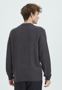 Temno siv pleten svetrov s krožnim izrezom, rebrastimi manšetami in robom. Ima gladko teksturo in sproščen kroj.