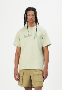 Light green cotton t-shirt with a crew neckline, featuring a green Nike logo design on the chest. Paired with tan cargo shorts.