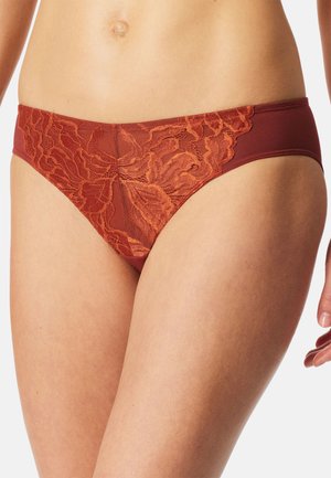 Close-up of a midsection wearing rust-colored lace bikini-style underwear with floral patterns on a light skin tone.