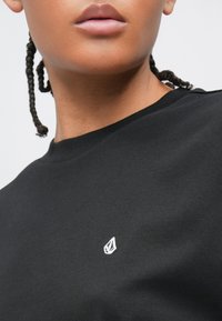 Μαύρο βαμβακερό T-shirt με στρογγυλή λαιμόκοψη και μικρό λευκό λογότυπο στην αριστερή πλευρά, με λεία υφή και κλασική εφαρμογή.