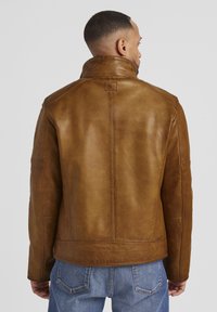 Braune Lederjacke mit hohem Kragen, die eine glatte Textur und eine dezente Maserung aufweist. Die Rückansicht zeigt ein stromlinienförmiges Design und detaillierte Nähte.