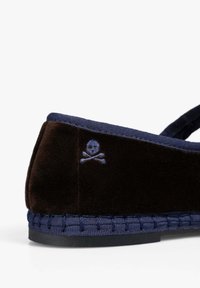 Zapato marrón de terciopelo tipo slip-on con ribete azul marino, que presenta un detalle bordado de una calavera y huesos cruzados en el lateral y una suela de tejido texturizado.