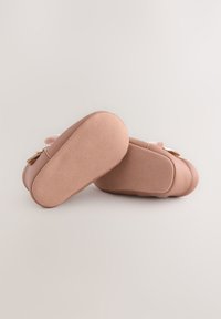 Chaussures bébé en cuir rose avec une semelle en daim souple, une forme arrondie et un nœud décoratif sur le côté. Texture lisse.
