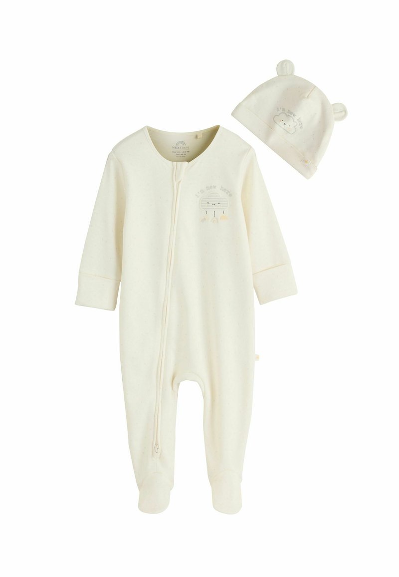 Kremasto obarvan dojenčkov pajac iz mehke tkanine, z zadrgo spredaj, dolgimi rokavi, pokritimi nogicami in ujemajočo kapo z medvedjimi ušesi.