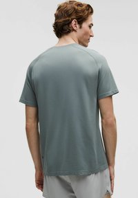 Lysegrå sports-t-shirt med tekstureret stof, kortærmet og med en afslappet pasform. Bagfra ses et enkelt design uden pynt.