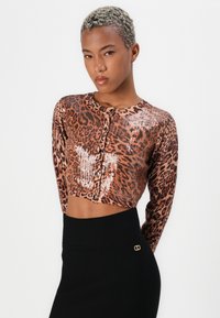 Cropped, long-sleeve cardigan in leopard print with sequins, featuring a round neckline and button closures. Paired with a black high-waisted skirt.