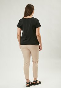 Top corto nero a maniche corte con cucitura posteriore, pantaloni beige aderenti e sandali neri con cinturini regolabili. Tessuto di superficie liscia.