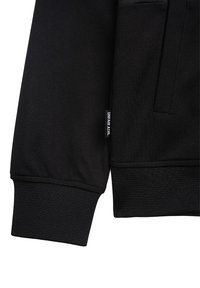 Svart sweatshirt med texturerad tyg, ribbade ärmslut och sidoficka. Etiketten på fållen säger "UNFAIR ATHL".