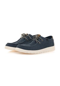 Zapatos de lona azul marino con suelas de goma blanca, superficie texturizada, punta redonda y cordones trenzados; presenta acentos en color tostado en el talón y los ojetes.