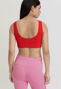 Rotes ärmelloses Crop-Top mit rundem Rücken, kombiniert mit hochtaillierten hellrosa Leggings aus glattem Stoff und mit minimalen Nähten.