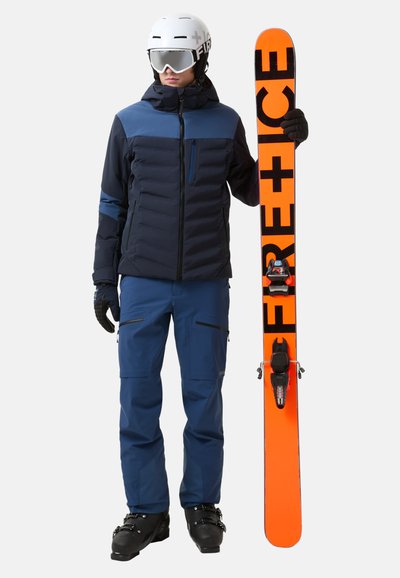 Ski-outfit met een marineblauwe pufferjack, blauwe broek, zwarte handschoenen en een witte helm. Houdt een oranje snowboard vast met zwarte letters.