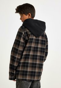 Sort og brun ternet skjorte med sort hætte, der har en knappestikdesign, lange ærmer og en blød stoftekstur.