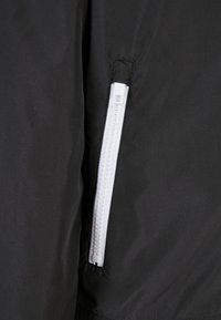 Fermeture éclair blanche sur tissu noir, partiellement fermée, avec des coutures visibles autour de la couture de la fermeture éclair.
