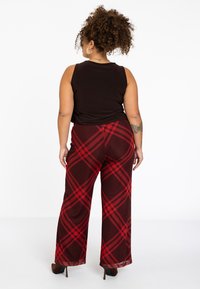 Wijduitlopende broek in een rood-zwart geruit patroon, gemaakt van een lichtgewicht stof. Gecombineerd met een zwart tanktop en hoge hakken.